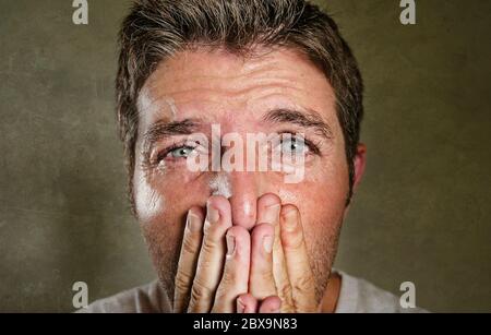 head and shoulders dramatic portrait of young man crying in pain suffering depression and anxiety problem covering his mouth with the hands feeling sa Stock Photo