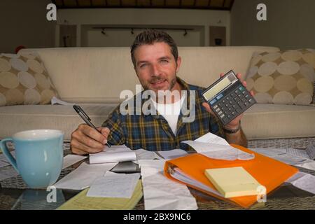 home lifestyle accounting portrait of young attractive and happy man counting monthly expenses and payments doing paperwork bills and calculator in do Stock Photo