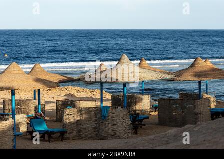 Red Sea beach with straw umbrellas and deck chairs near Marsa Alam, Egypt, Africa. The waves of the sea crash on the coral reef Stock Photo