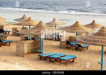 Red Sea beach with straw umbrellas and deck chairs near Marsa Alam, Egypt, Africa. The waves of the sea crash on the coral reef Stock Photo