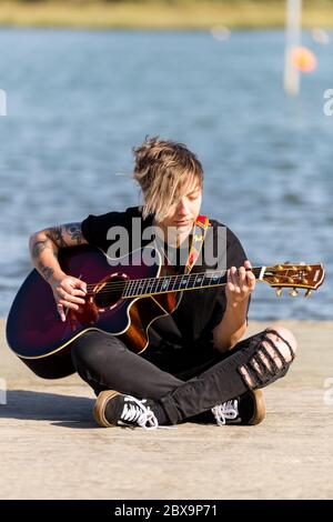 Woodbridge, Suffolk, UK September 20 2020: A 20 something female relaxing and playing an acoustic guitar outside for passers by to listen too Stock Photo