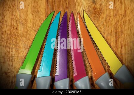 Close-up of set of six colored table knives on a wooden cutting board Stock Photo