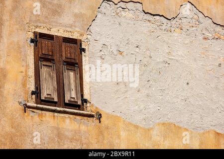 Close-up of an old window with closed brown wooden shutters on an orange broken wall. Trentino-Alto Adige, Italy, Europe Stock Photo
