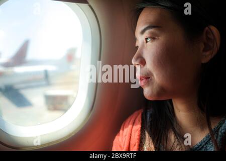 young happy and beautiful Asian Korean tourist woman smiling excited sitting in airplane by the window arriving destination in aircraft transportation Stock Photo