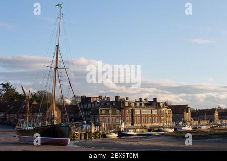 The Blakeney Hotel and the waterfront, Blakeney, with the sailing barge 'Juno' moored at low tide on Agar Creek, Blakeney, Norfolk, England Stock Photo