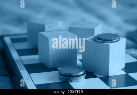 Coins on chess board and wooden cubes, concept business background. Image toned to classic blue Stock Photo