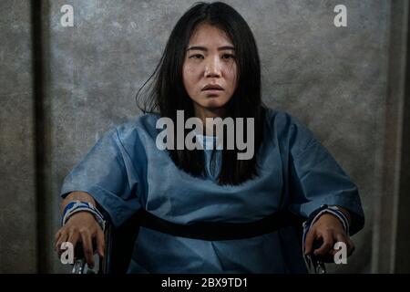 young crazy and mentally insane Asian woman restrained in wheelchair at mental hospital suffering psychiatric disorder as schizophrenia looking catato Stock Photo