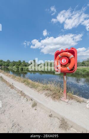 Sunlit bright orange-red lifebuoy ring in quayside housing on River Fowey at Lostwithiel. For safety, danger, staying afloat, possibly risk assessment Stock Photo