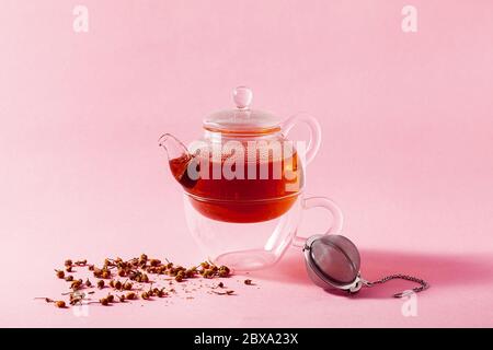 tea in a glass teapot on a pink background and a metal Infuser Filter Stock Photo