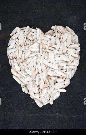 Organic yellow sunflower seeds in heart shape on black background Stock Photo