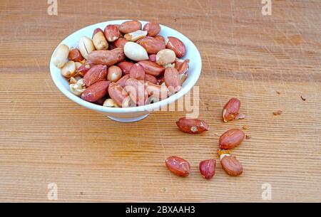 Plateful of Organic unsalted peanuts and Spilled unsalted peanuts on Wooden Background Stock Photo