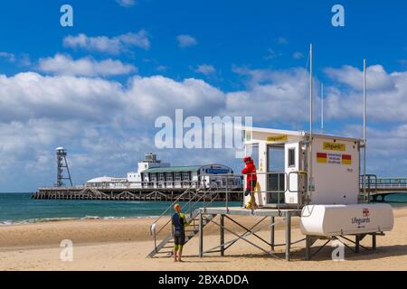 Swimmer talks to RNLI Lifeguard at kiosk hut near Bournemouth Pier on cool windy day at Bournemouth, Dorset UK in June Stock Photo