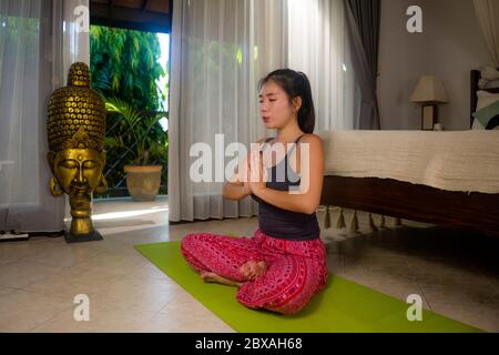 yoga against lockdown quarantine stress - young beautiful and happy Asian Korean woman doing yoga workout at home bedroom practicing relaxation and me Stock Photo