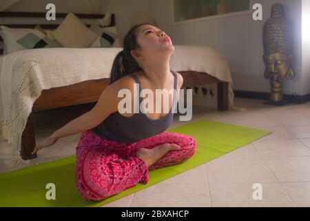 yoga against lockdown quarantine stress - young beautiful and happy Asian Korean woman doing yoga workout at home bedroom practicing relaxation and me Stock Photo