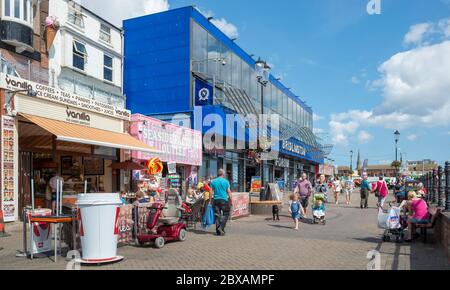 People walking past shops and an amusement arcade on the promenade at Bridlington, East Yorkshire Stock Photo