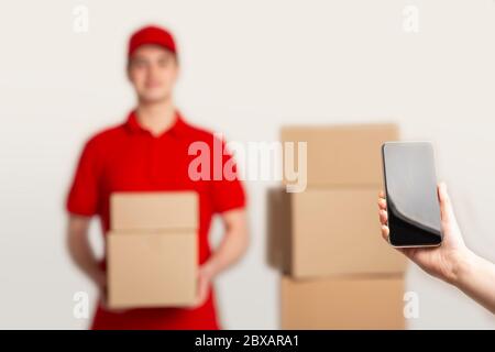 Female hand holds smartphone with blank screen close up, deliveryman holds boxes Stock Photo