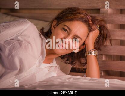 portrait of attractive happy and beautiful mature woman aged 50s to 60s smiling cheerful and charming at home bedroom sitting on bed in the morning in Stock Photo
