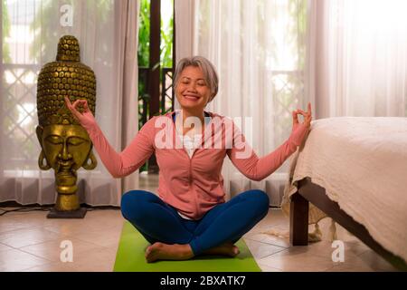 home lifestyle - beautiful and happy mature woman with gray hair on her 50s doing yoga and meditation exercise at Asian deco bedroom feeling peaceful Stock Photo