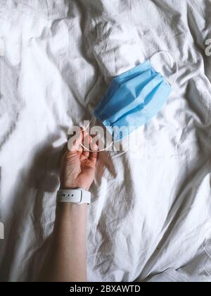 Protective medicine mask on bed with hand. Personal protective equipment, environmental pollution, new normal concept Stock Photo