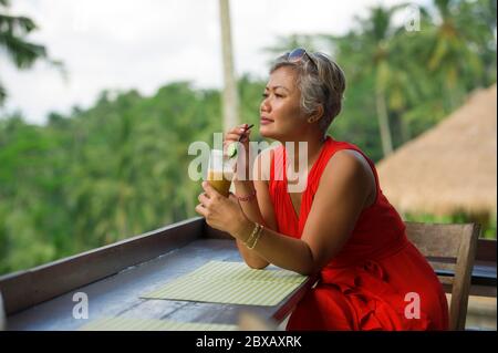 natural lifestyle outdoors portrait of attractive and happy middle aged Asian Indonesian woman in stylish red dress enjoying tropical holiday trip at Stock Photo