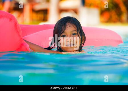 lifestyle outdoors portrait of young happy and cute female child having fun with inflatable airbed in holidays resort swimming pool smiling carefree a