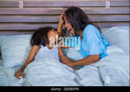 lifestyle bedroom portrait of happy Asian woman at home playing with little daughter in bed cuddling and laughing cheerful in mother and child love an Stock Photo