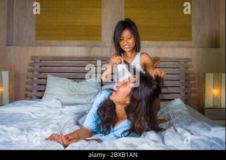 lifestyle bedroom portrait of happy Asian woman at home playing with little daughter in bed cuddling and laughing cheerful in mother and child love an Stock Photo