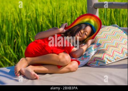 sweet happy and beautiful 7 or 8 years old child in Summer hat and cute red dress having fun outdoors smiling cheerful lying on resort pool bed at ric