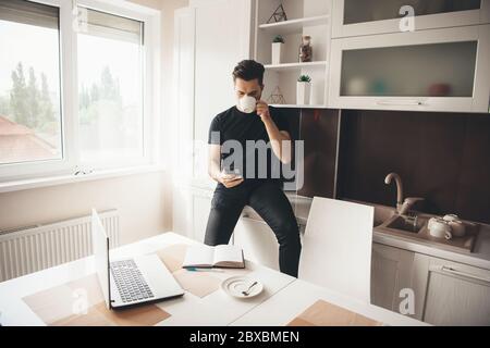 Young caucasian programmer is having a break drinking a coffee and chatting on phone in the kitchen Stock Photo