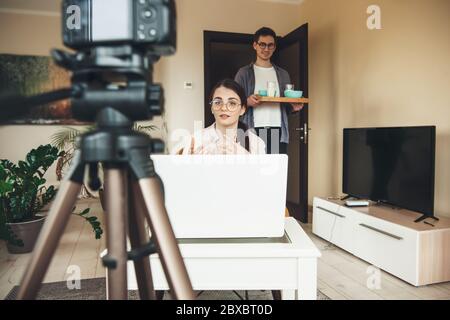 Cute caucasian woman having online lessons is explaining something while her lover is brinking the breakfast Stock Photo