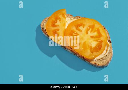 slice of bread with yellow tomato isolated on blue background, top view Stock Photo