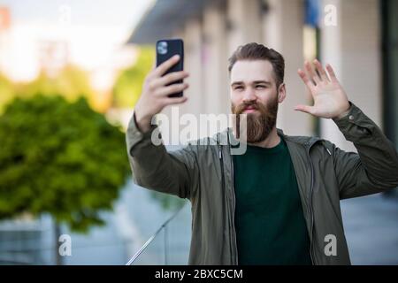 Hi there. Man smiling taking selfie photo smartphone urban background. Streaming online video call. Mobile internet. Hipster mobile phone. Stock Photo