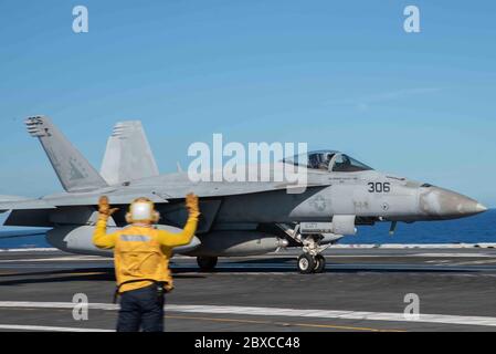 U.S. Navy yellow jacket signals a F/A-18E Super Hornet fighter aircraft, attached to Eagles of Strike Fighter Squadron 115, after landing on the flight deck of the Nimitz-class aircraft carrier USS Ronald Reagan June 2, 2020 underway in the Philippine Sea. Stock Photo