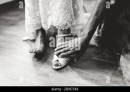 Black and white closeup photo of male hand touching brides foot wearing white shoe. Wedding day concept. Stock Photo