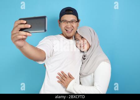 Portait of happy Asian muslim couple making selfie and smiling, husband and wife hugging full of love, family concept Stock Photo