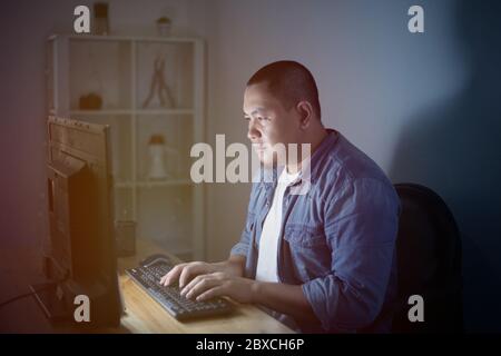 Young Asian businessman entrepreneur working overtime alone in a dark office at the evening, work hard for his ambition of success Stock Photo