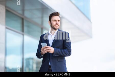 Handsome financier in business suit browsing web on his smartphone outdoors Stock Photo