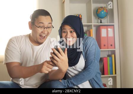 Asian muslim couple smiling happy when looking at smart phone, good news on internet concept Stock Photo