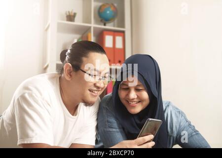 Asian muslim couple smiling happy when looking at smart phone, good news on internet concept Stock Photo
