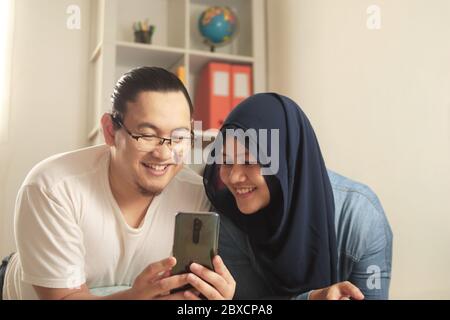 Asian muslim couple smiling happy when looking at smart phone, good news on internet concept Stock Photo