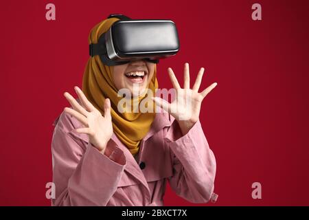 Happy young Asian muslim girl wearing hijab playing on VR glasses. Virtual reality concept with young girl having fun with headset goggles Stock Photo