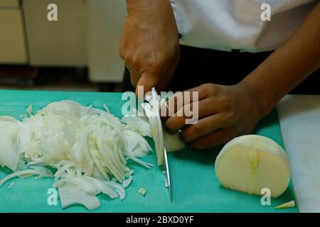 a chef slicing white onion on a green choping board Stock Photo