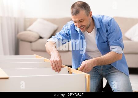 Happy Man Fixing Furniture Using Screwdriver Sitting On Floor Indoor Stock Photo