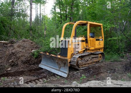 A John Deere 450G crawler dozer parked on a logging road in the Adirondack Mountains, NY USA wilderness Stock Photo