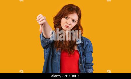 Millennial Girl Gesturing Thumbs Down Over Yellow Studio Background, Panorama Stock Photo