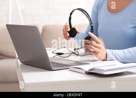 Beginning of working day of online consultant. Woman holds headphones in her hands, near laptop and notebook on table Stock Photo