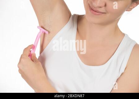 Beautiful young woman in a white T-shirt is smiling and doing a depilation of armpits or shaving underarms pink razor on a white background Stock Photo