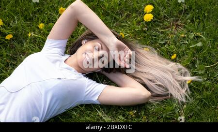 Woman lies on green grass relaxing outdoors looking happy and smiling Stock Photo