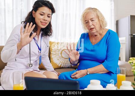Doctor visiting senior patient at home and using telemedicine service to consult cardiologist Stock Photo