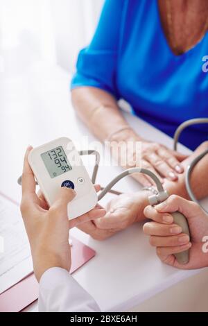 Hands of general practitioner using electronic tonometer when checking blood pressure of senior woman Stock Photo